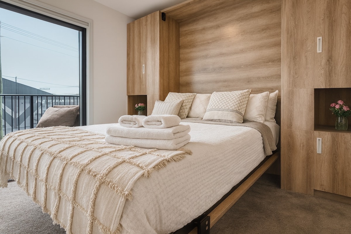 Cozy modern bedroom with soft linens, wooden cabinetry and balcony view at the Blissful Studio