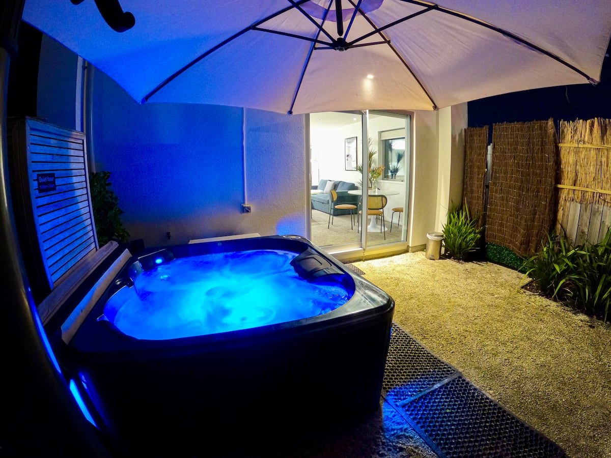 Nighttime view of the private blue-lit hot tub with the warm living room glowing beyond at Central City Heaven Spa
